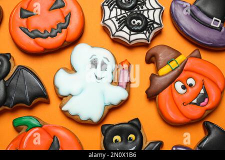 Biscotti di pan di zenzero decorati in modo diverso su fondo arancione, giacitura piatta. Festa di Halloween Foto Stock