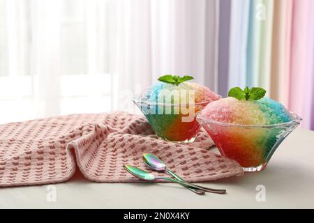 Ghiaccio da barba arcobaleno in ciotole di vetro da dessert e cucchiai su un tavolo di legno all'interno Foto Stock