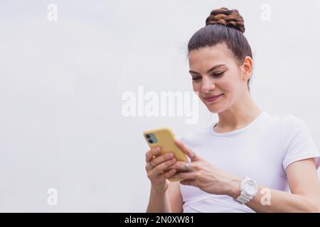 Giovane brunetta Donna che usa l'app per telefono cellulare prima di correre nel parco. Blogger sportivo attivo femminile caucasica che utilizza i social media e la trasmissione in streaming Foto Stock