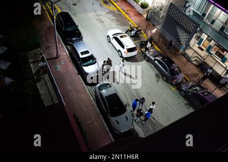 Foto notturna di strada da un tetto che guarda giù a due gruppi di giovani sulle strade di South Beach. Foto Stock