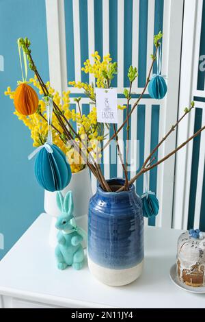 Vasi con bella decorazione di Pasqua, fiori mimosa e coniglietto giocattolo sul tavolo vicino al muro di colore, primo piano Foto Stock