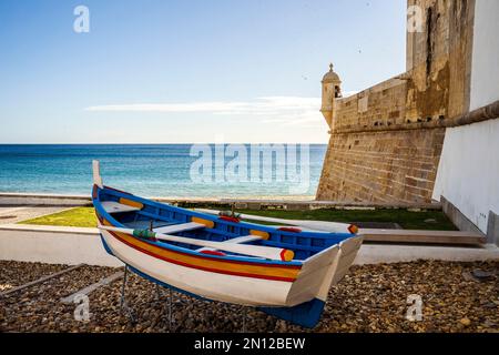 La barca tradizionale in legno e la Fortezza di San Giacomo sulla spiaggia di Sesimbra, l'area metropolitana di Lisbona, Portogallo, Europa Foto Stock