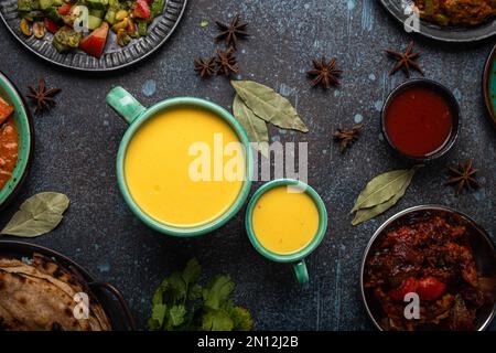 Sani Ayurveda indiano bere mango lassi in due tazze su rustico tavolo di cemento con altri alimenti indiani dall'alto, bevanda mista gialla fatta di mang Foto Stock
