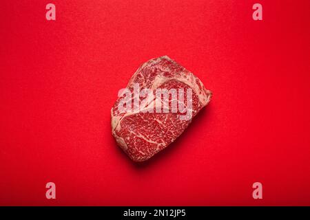 Carne cruda fresca cruda di manzo bistecca di prima qualità Ribeye su sfondo rosso pulito dall'alto, beefsteak concetto banner minimalismo Foto Stock