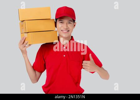 Giovane asiatico in rosso uniforme e cappello in piedi per il trasporto della scatola stack e pollici su sfondo bianco isolato, il dipendente stiva carico, corriere e consegna, Foto Stock