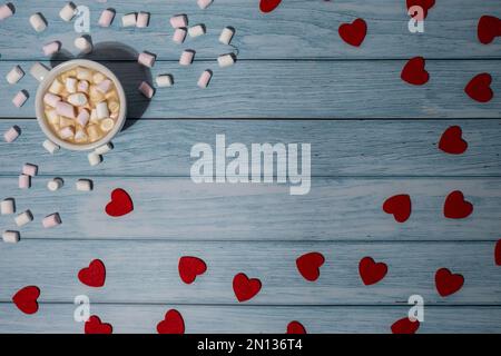 Saluto o invito mock up con cuori rossi con tazza bianca di caffè e marshmallows su sfondo di legno blu. Romantico piccolo cuore San Valentino. Spazio vuoto per la copia della scheda di carta per il testo. Mattina delle vacanze. Vista dall'alto, piatto stile minimalista estetica lusso bohémien business branding concetto Foto Stock