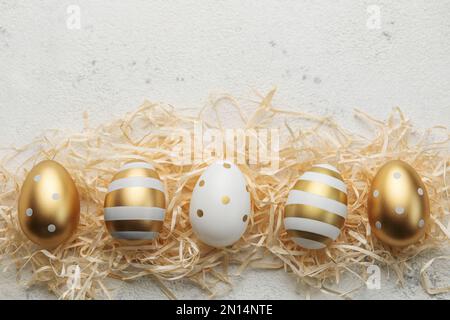 Uova di Pasqua dipinte con vernice d'oro su fondo paglierino. Concetto di vacanze di Pasqua. Sfondo festivo. Foto Stock