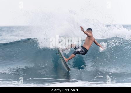 Uomo che naviga in onda con una tavola da surf a Keramas Beach, Bali, Indonesia. Ragazzo surfista sulla spiaggia di sabbia nera e uluwatu Foto Stock