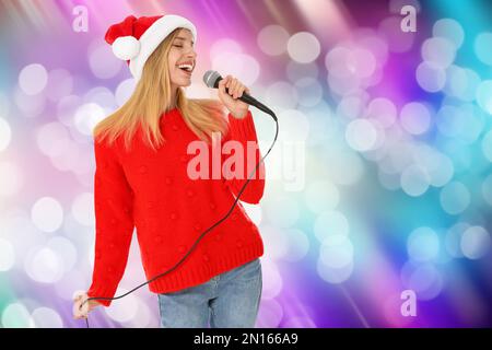 Donna felice in Babbo Natale che canta su sfondo luminoso, effetto bokeh Foto Stock