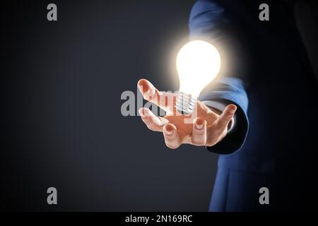 Concetto di idea. Uomo d'affari che mostra la lampadina luminosa illustrazione su sfondo scuro, primo piano Foto Stock