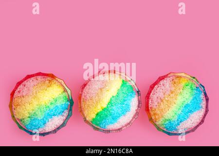 Rasatore di ghiaccio arcobaleno in ciotole di vetro da dessert su sfondo rosa, piatto. Spazio per il testo Foto Stock