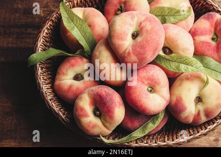 Pesche di ciambella fresche mature in cesto su tavolo di legno, vista dall'alto Foto Stock