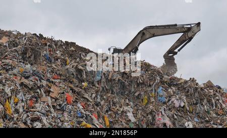 Un escavatore che lavora in una discarica vicino alla città. Foto Stock