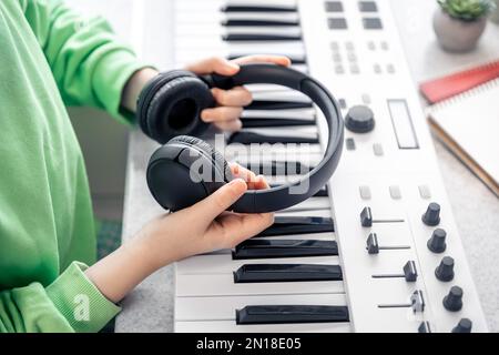 Primo piano, cuffie nelle mani di un bambino sullo sfondo del pianoforte. Foto Stock