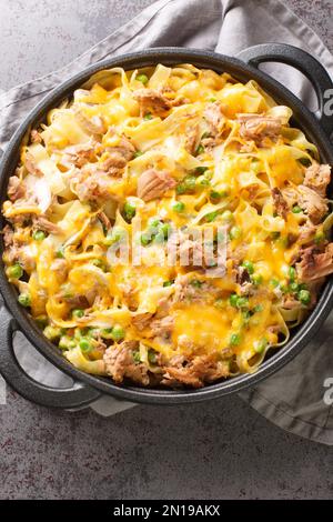 Casseruola di tonno con tagliatelle, piselli verdi, funghi e formaggio cheddar primo piano in una teglia da forno sulla tavola. Vista verticale dall'alto Foto Stock