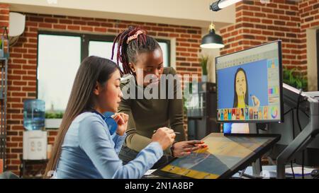 Un team di coloristi diversi che modifica immagini con interfaccia di ritocco, lavorando alla classificazione dei colori delle foto. Artisti di agenzie creative che modificano le immagini su software di produzione, facendo lavoro di squadra. Foto Stock