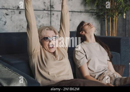 Donna anziana entusiasta che gioca ai videogiochi, ha in mano un controller che fa un gesto da winnner. Concetto di nonna sconfiggere il videogioco. Foto Stock