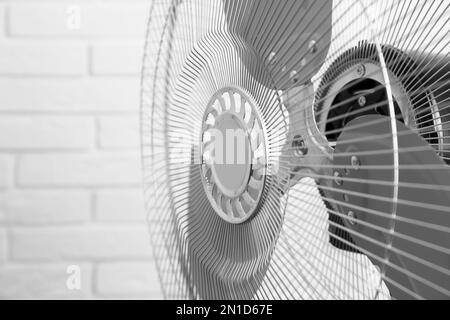 Ventilatore elettrico vicino a muro di mattoni bianchi, primo piano. Caldo estivo Foto Stock