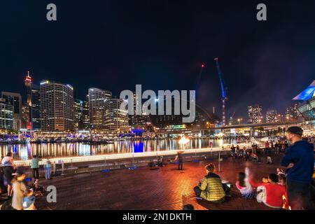 Sydney, Australia - 16 aprile 2022: Spettacolo di strada al Darling Harbour mentre illuminato il quartiere degli affari di Sydney City visto sullo sfondo Foto Stock