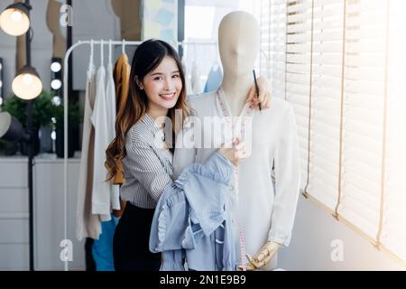 Un bel seamstress con capelli lunghi scrive in un notebook. il sarto crea una collezione di abiti. giovane donna designer vestiti appunti idee in no Foto Stock