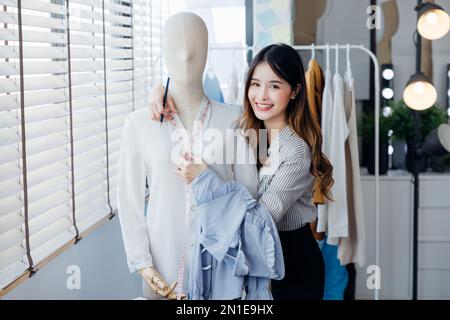 Un bel seamstress con capelli lunghi scrive in un notebook. il sarto crea una collezione di abiti. giovane donna designer vestiti appunti idee in no Foto Stock