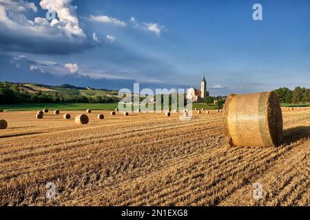 Campagna italiana con un campo pieno di balle di fieno e una chiesa sullo sfondo, Emilia Romagna, Italia, Europa Foto Stock