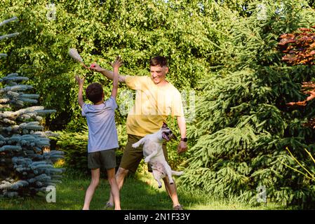 Ridendo padre e figlio che giocano all'aperto con un cane da compagnia di famiglia Foto Stock