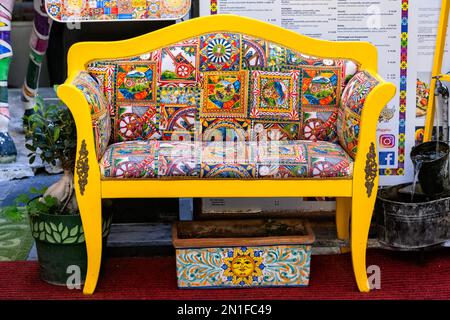 Taormina Sicilia Italia, panchina di colore giallo brillante con colorate patchwork coperture all'esterno di un ristorante nel centro storico di Taormina Foto Stock