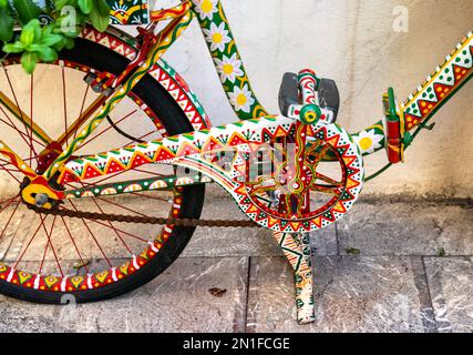 Primo piano catena e ruota ciclabile dipinte con colori vivaci nel centro storico di Taormina, Sicilia, Italia Foto Stock