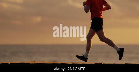 Foto dell'uomo in forma che corre lungo la riva dell'oceano al mattino. Sano jogging maschile sulla spiaggia Foto Stock