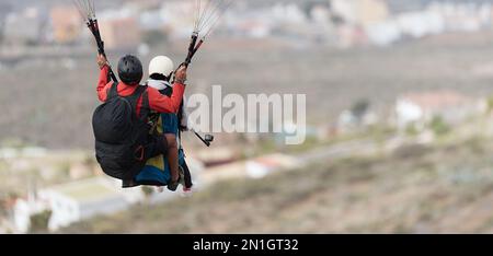 Volare parapendio tandem sopra la città in una giornata di sole Foto Stock