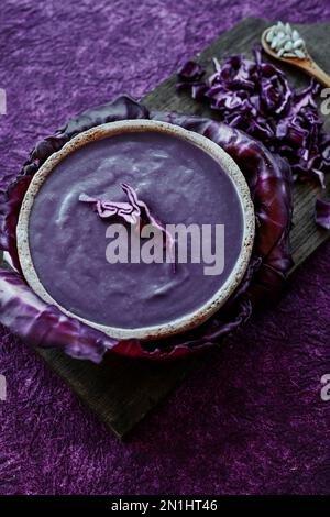 vista ad angolo alto di una zuppa di cavolo rosso in una rustica ciotola in ceramica, posta su una superficie ruvida viola Foto Stock