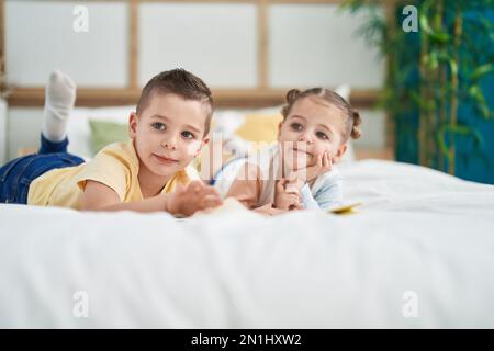 Due bambini che leggono un libro di storia sdraiato sul letto in camera da letto Foto Stock