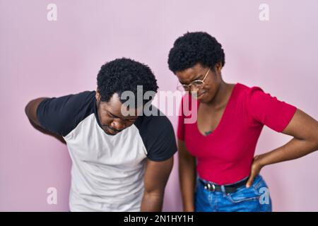 Giovane coppia afro-americana in piedi su sfondo rosa sofferenza di mal di schiena, toccare la schiena con la mano, dolore muscolare Foto Stock