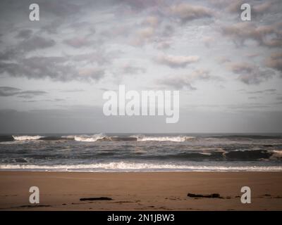 Oceano Atlantico in una pallida giornata invernale. Vista frontale delle onde sulla spiaggia vuota e cielo grigio nuvoloso Foto Stock