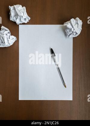 Piatto con foglio di scrittura vuoto, penna e palline di carta stropicciate sulla parte superiore della scrivania di legno per ufficio. Il blocco del produttore o concetto di crisi di creatività. Vista dall'alto Foto Stock