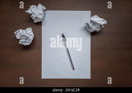 Piatto con foglio di scrittura vuoto, penna e palline di carta stropicciate sulla parte superiore della scrivania di legno per ufficio. Il blocco del produttore o concetto di crisi di creatività. Vista dall'alto Foto Stock