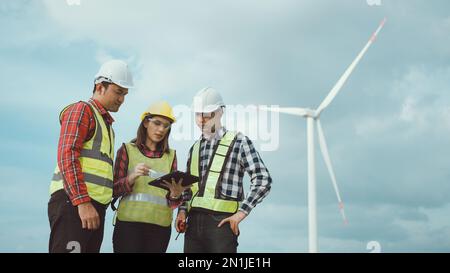 Team di ingegneri asiatici che discutono e controllano le turbine nella fattoria di turbine eoliche. Tecnologia e sostenibilità delle energie rinnovabili. Foto Stock