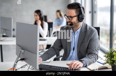 Simpatico e sorridente operatore giovane di call center maschile che lavora nel servizio di assistenza clienti Foto Stock