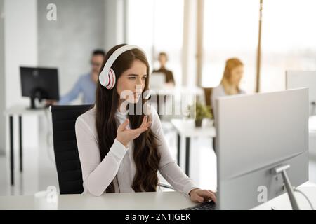 Operatore femminile dedicato che cerca di risolvere problemi tecnici mentre parla con un cliente nel settore dell'assistenza IT Foto Stock