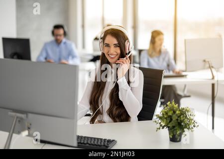 Attraente agente di affari donna in camicia bianca indossando cuffie bianche presso il call center Foto Stock
