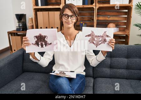 Brunette donna che lavora con rorschach test in psicologia clinica sorridendo guardando al lato e fissando via il pensiero. Foto Stock