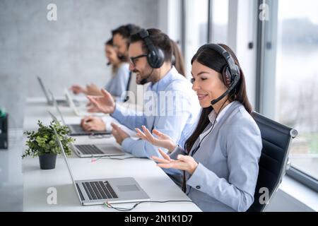 Ritratto di una giovane e amichevole operatore di call center femminile in cuffie che lavorano con i suoi colleghi al centro di assistenza clienti. Foto Stock