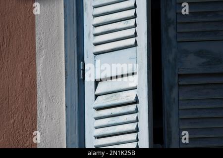 Vecchia casa rurale persiane in legno blu chiaro con finiture bianche su una parete di stucco veneziano. Foto Stock