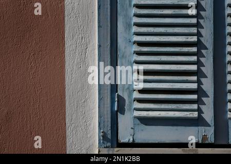 Vecchia casa rurale persiane in legno blu chiaro con finiture bianche su una parete di stucco veneziano. Foto Stock