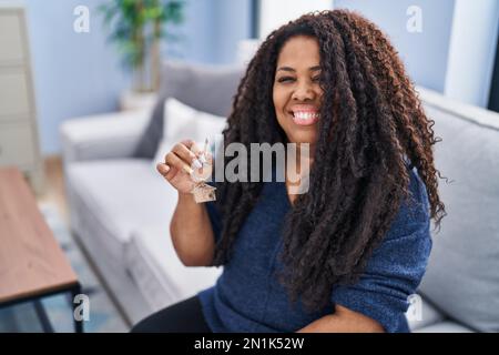 Più dimensione donna ispanica tenendo le chiavi di nuova casa guardando positivo e felice in piedi e sorridente con un sorriso sicuro mostrando i denti Foto Stock