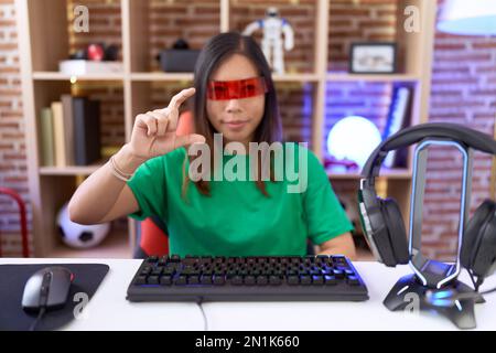 Donna cinese di mezza età che indossa occhiali di realtà virtuale sorridente e sicuro gesturing con mano facendo segno di piccolo formato con le dita che guardano e il Foto Stock