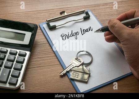 Focalizzazione selettiva di calcolatrice, chiave della casa, e scrittura a mano prestito ponte su una clipboard con white paper. Foto Stock