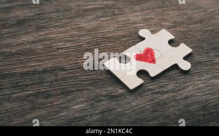 Messa a fuoco selettiva di due pezzi di un puzzle che forma un cuore su uno sfondo rustico di legno con spazio copia. Concetto di amore. Foto Stock