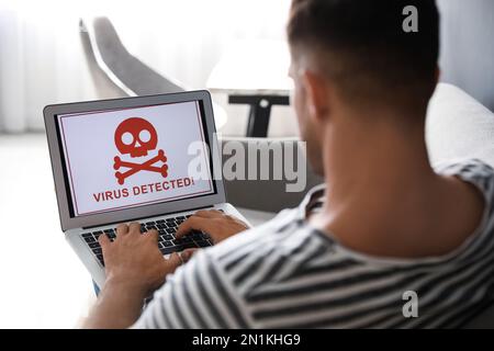 Uomo che utilizza un computer portatile con avviso di attacco di virus a casa Foto Stock